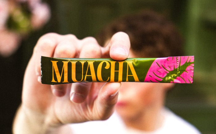 Hand holding a Muacha matcha stick pack toward the camera